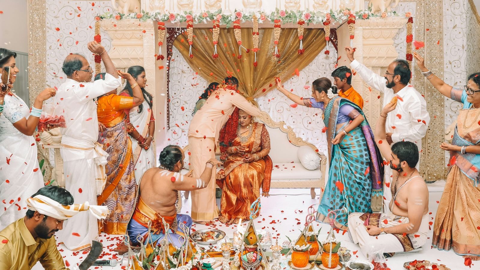 Individuals in traditional Indian clothing are engaged in a ritual with various items arranged on the floor.