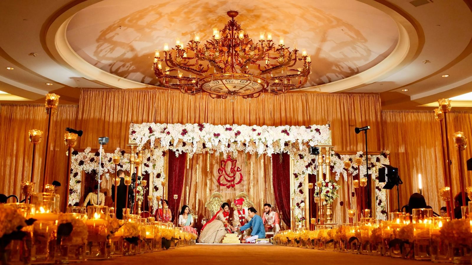 An elaborate wedding stage with floral decorations is set up in a grand hall.