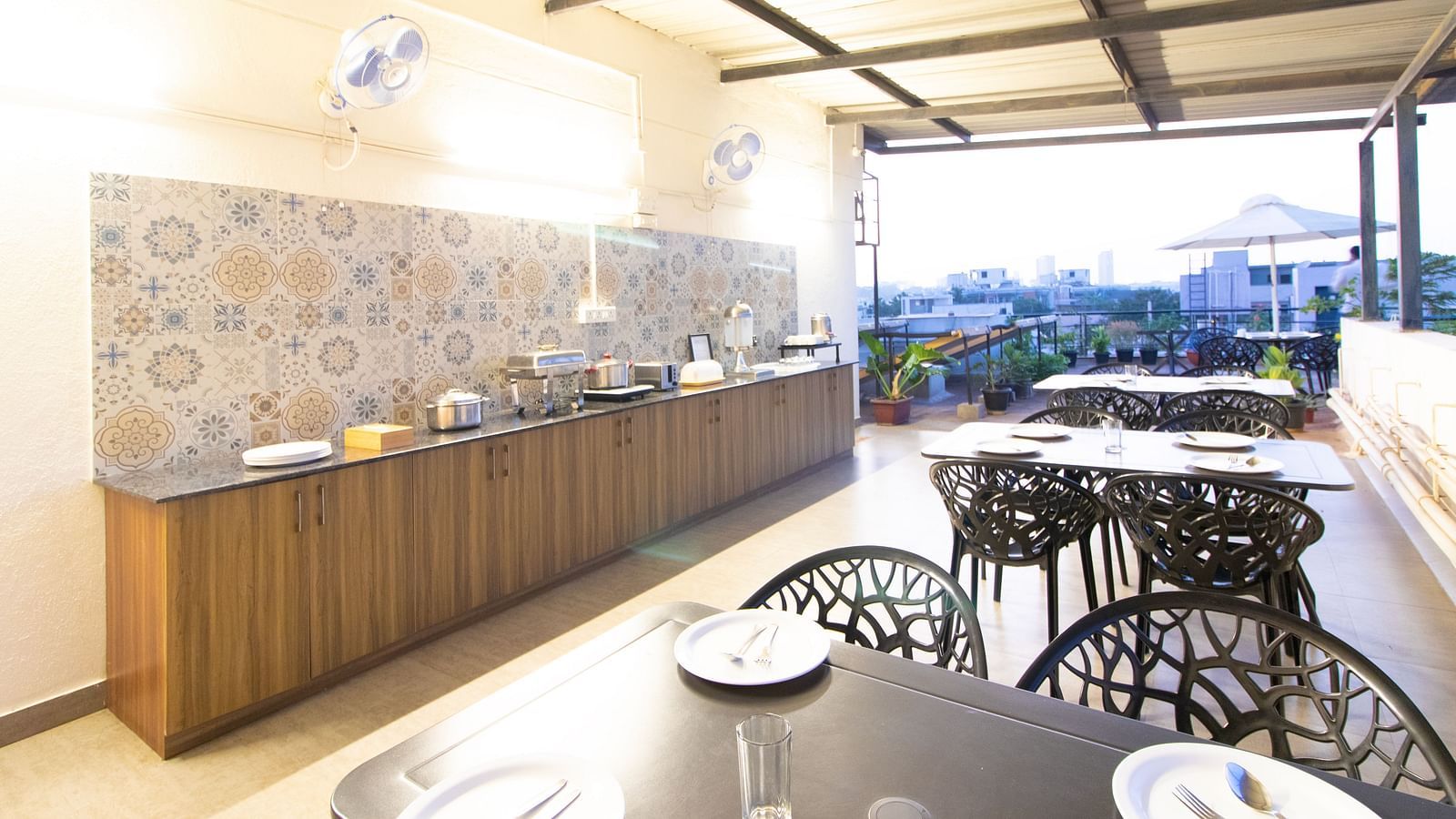 A dining space with tables and chairs under a partial roof, featuring a buffet setup along one side at Sanctum Suites Indiranagar, Bangalore.
