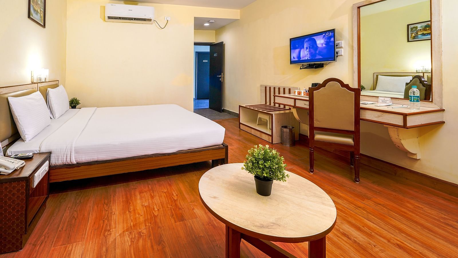Spacious hotel room with a double bed, wooden flooring, flat-screen TV, and work desk in Hyderabad near Ramoji Film City.
