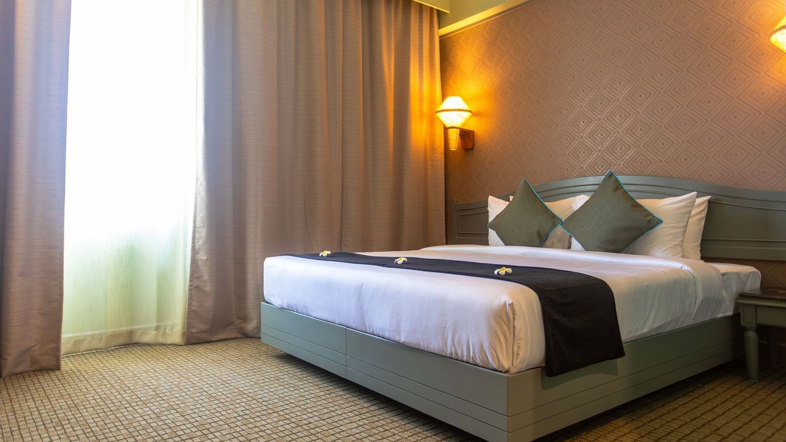 A bedroom at Shilton International, Kochi, with a large bed, warm lighting, and privacy curtains.