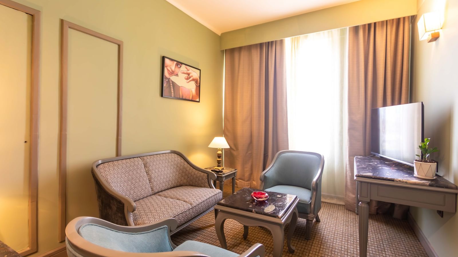  A sitting area at Shilton International, Kochi, with a sofa, two armchairs, and a well-lit window.