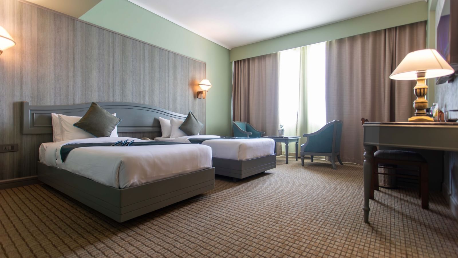 A hotel room at Shilton International, Kochi, with two beds, a sitting area, and ample natural light.