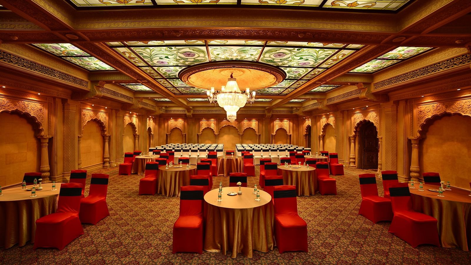 Seating arrangement in Taj Mahal Hall A grand hotel suite with an opulent red and white decor, large bed, and seating area, reflecting a traditional style at Sitara Luxury Hotel in Hyderabad near Ramoji Film City.
