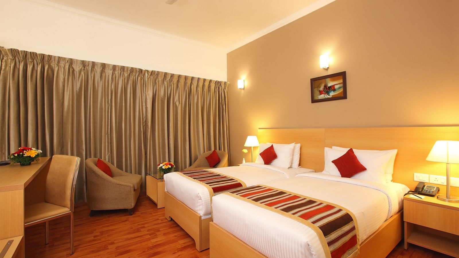 Twin beds inside Premium Room at Starlit Suites, Kochi features two single beds, a desk, an armchair, and warm, inviting lighting.