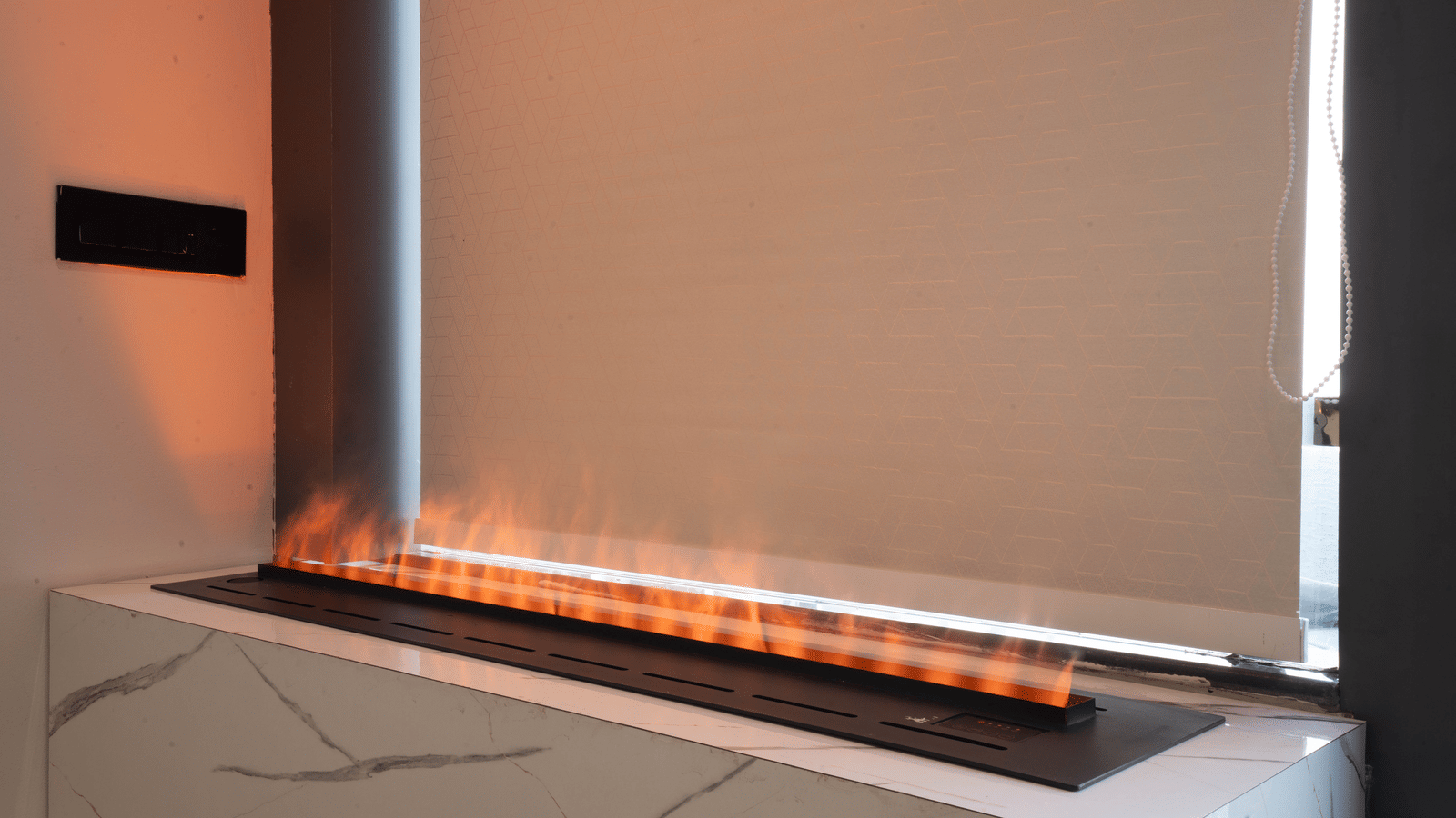 A modern linear gas fireplace with bright orange flames sits on a white marble base in a room at Sukoon by the Ganges.