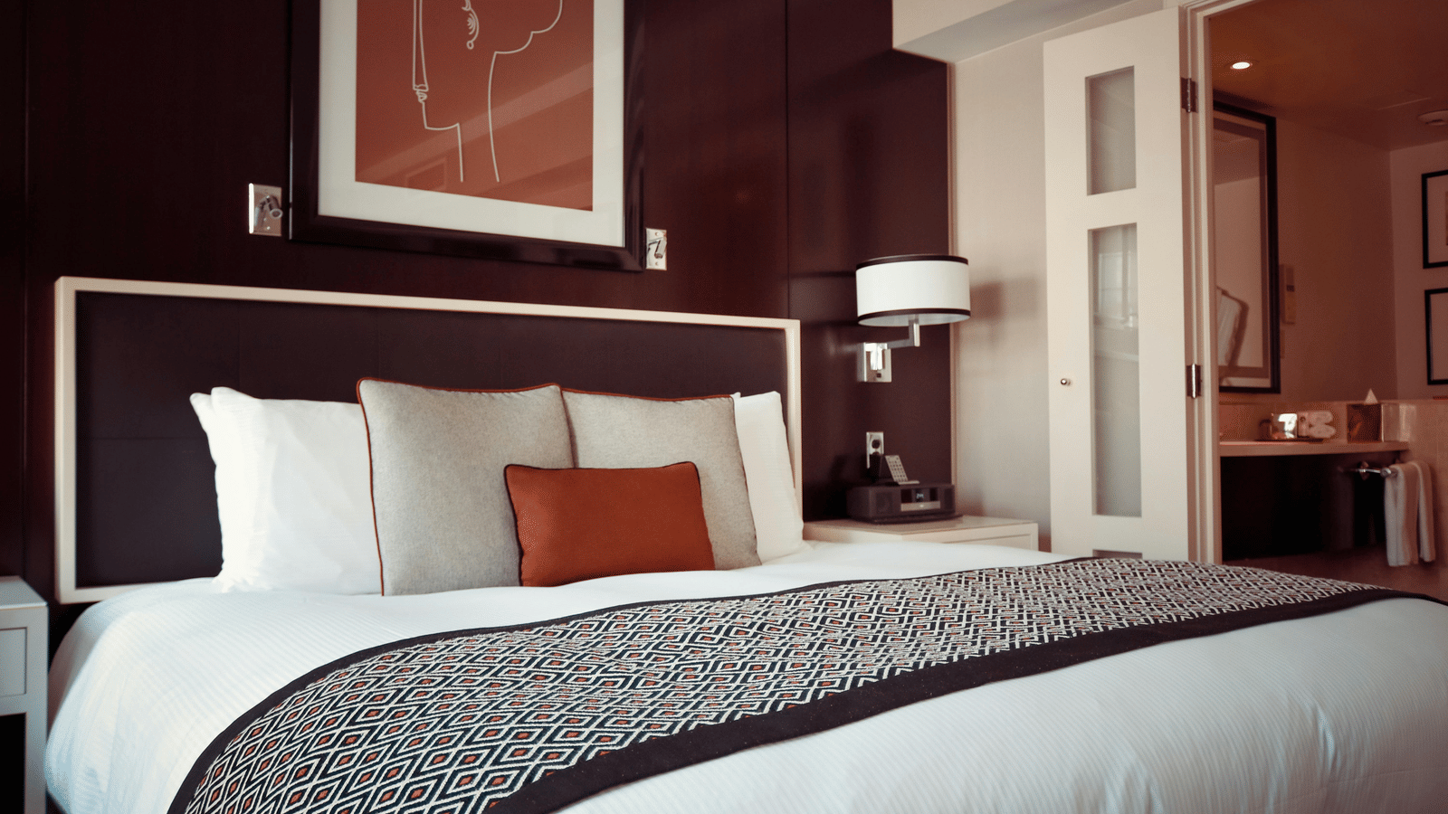 A  hotel room with a large bed, dark wood walls, and a modern, patterned grey bed runner.