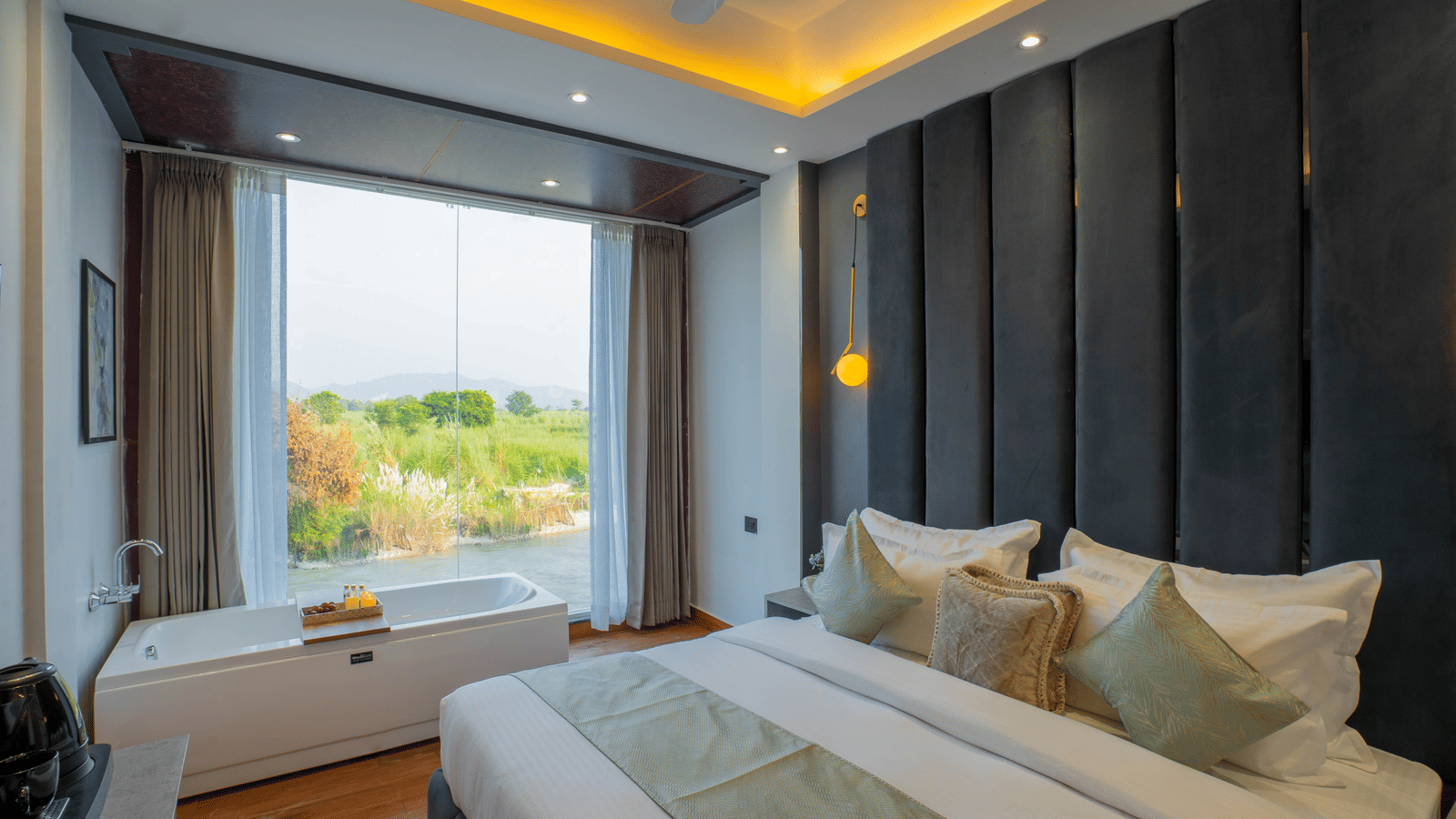 A guest room at Sukoon by the Ganges featuring a large bed and a soaking tub positioned in front of a wide river-view window.
