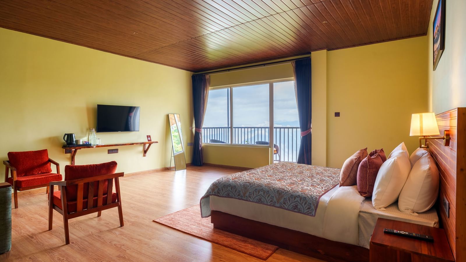 Bright bedroom with a double bed, TV, seating area, and large windows offering natural light.