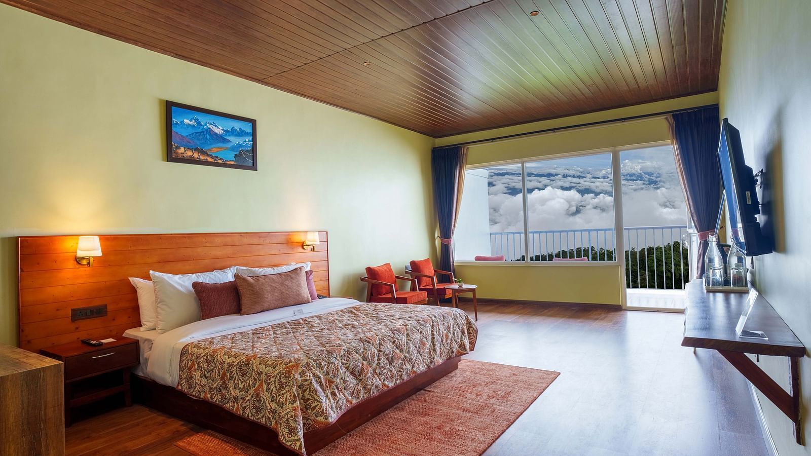 A tastefully decorated hotel room at Summit Enigma Resort & Spa, Lamahatta, with a large bed, a television, and a balcony offering an outdoor vista.