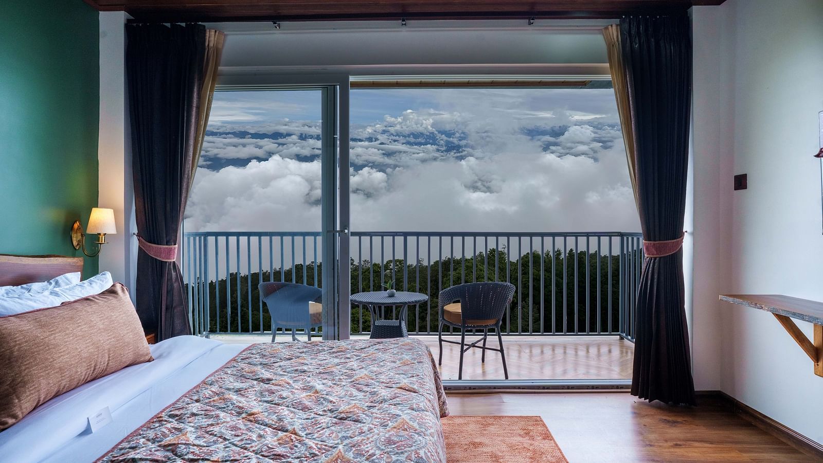 A spacious hotel room at Summit Enigma Resort & Spa, Lamahatta, with a large bed, a balcony overlooking a scenic view, and a modern interior design.