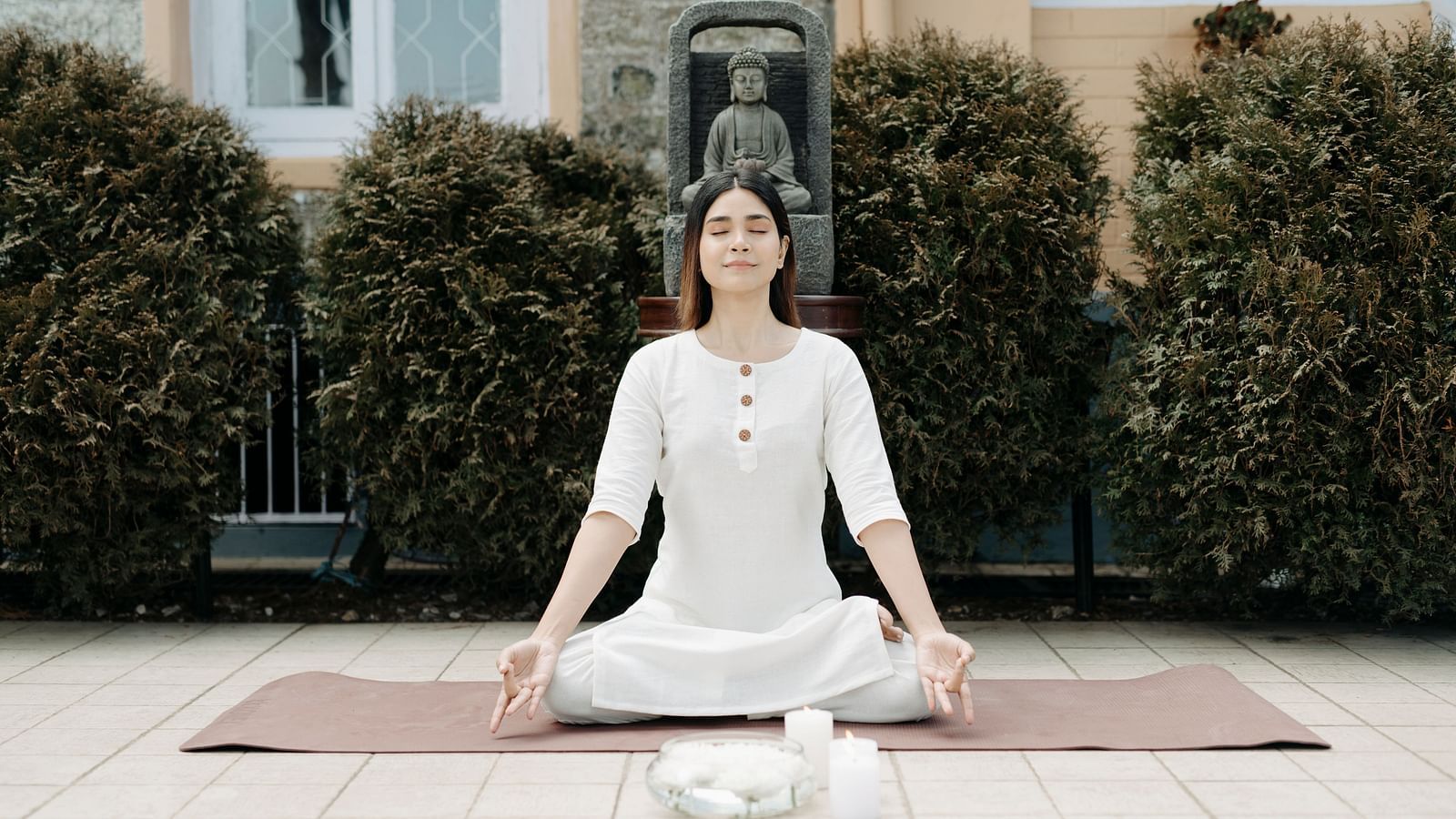 Woman practicing Pranayama yoga seated on the floor with green plants in the background