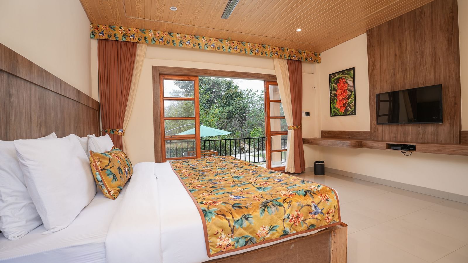 Bungalow featuring a spacious bed with a wall-mounted television, painting and a large balcony at Summit Green Lake Tea Resort & Spa, Kaziranga