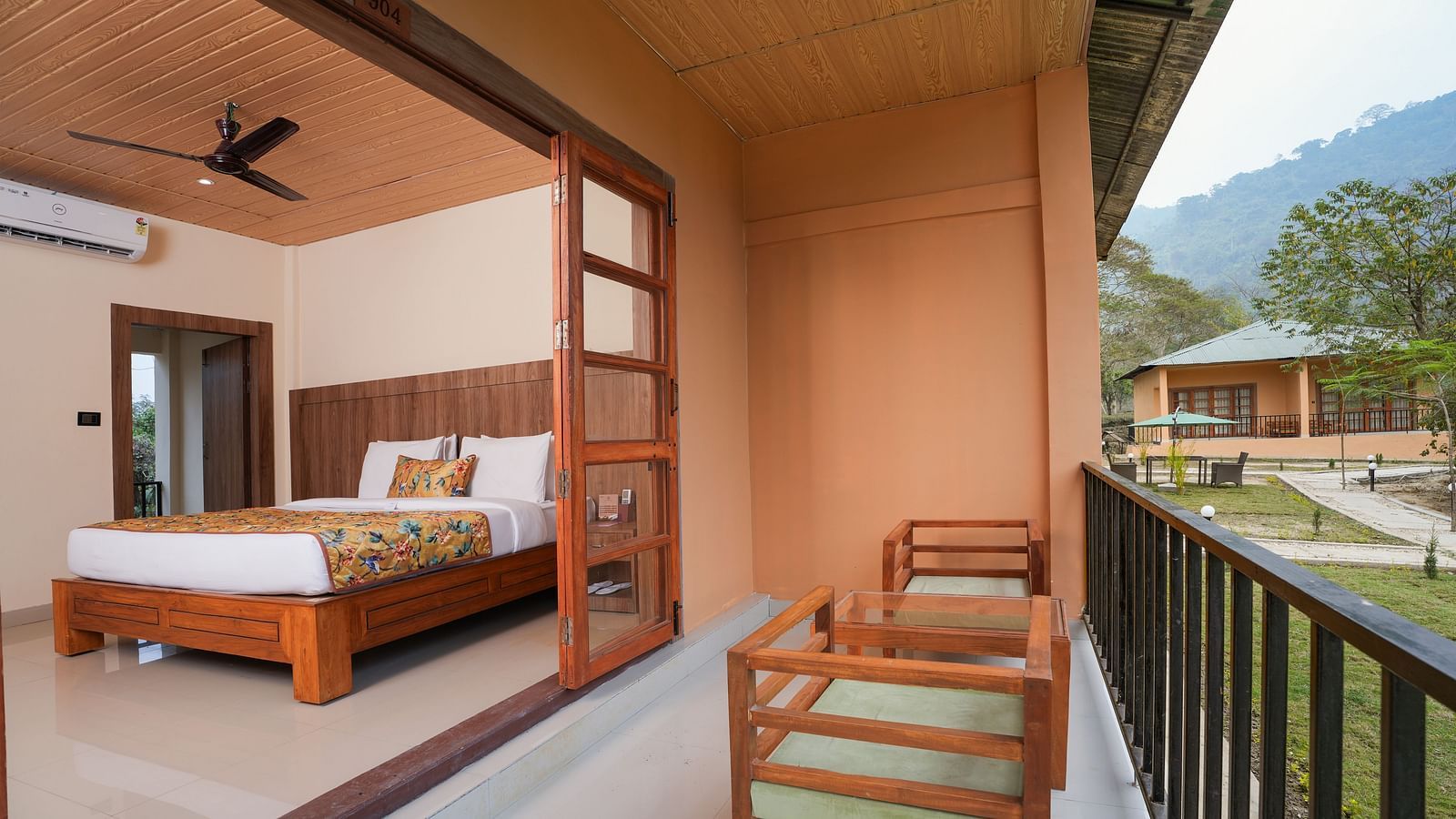 Bungalow featuring a spacious bed with wooden headboards, bedside table, air conditioning, and a large balcony at Summit Green Lake Tea Resort & Spa, Kaziranga
