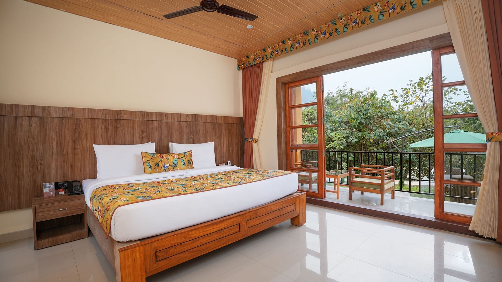 Bungalow featuring a spacious bed with wooden headboards, bedside table, and a large balcony at Summit Green Lake Tea Resort & Spa, Kaziranga