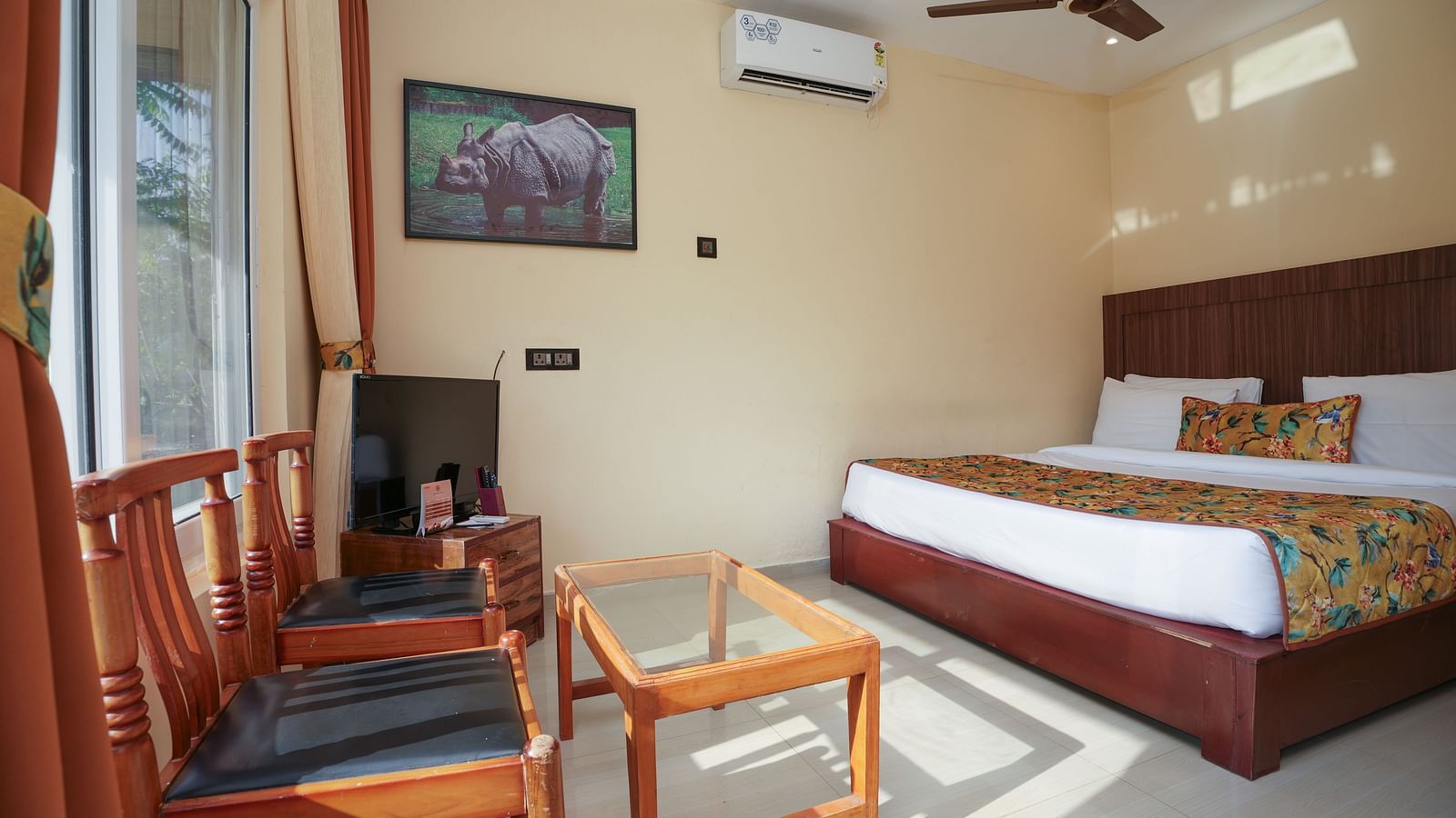 Deluxe Cottage featuring a spacious bed, television, air conditioner, glass table, and chairs at Summit Green Lake Tea Resort & Spa, Kaziranga