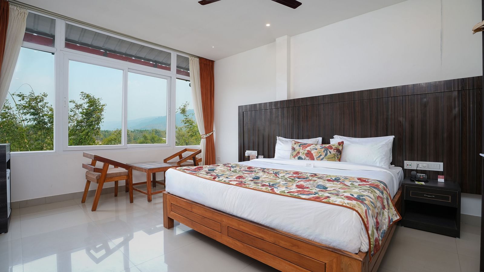 Deluxe room featuring large windows with a nature view, a spacious bed, air conditioning, wooden storage units, and a television at Summit Green Lake Tea Resort & Spa, Kaziranga4