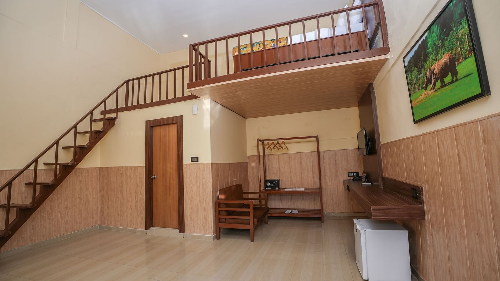 Duplex room with balcony features a living area with wooden furniture, a wine fridge, wall-mounted television, and stairs leading to the spacious bedroom at Summit Green Lake Tea Resort & Spa, Kaziranga