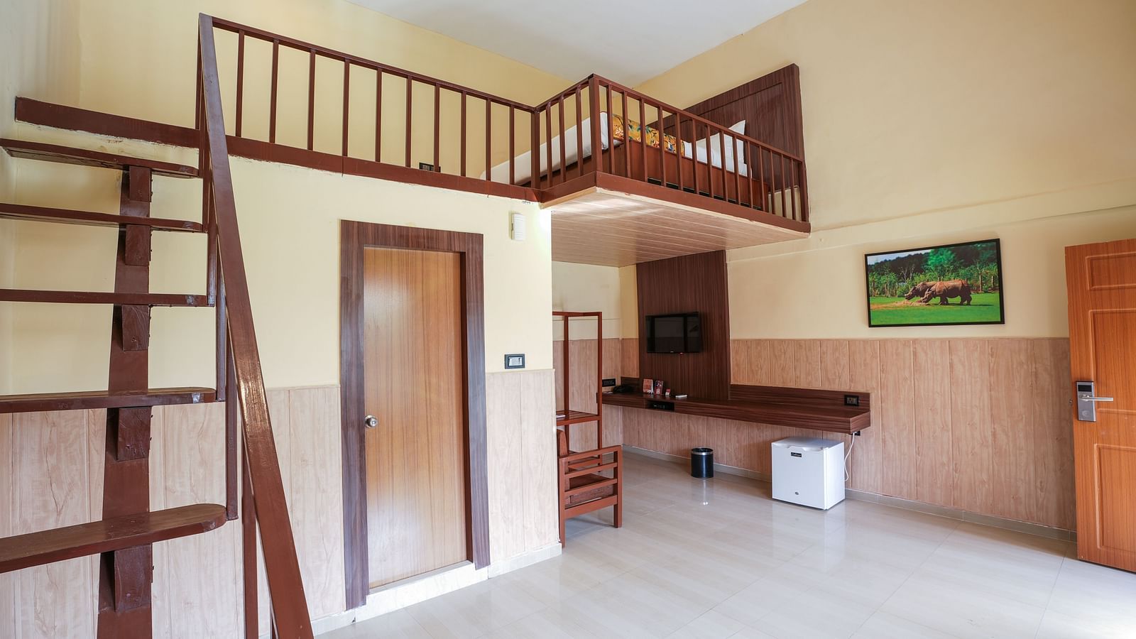 Duplex room with balcony features a living area with wooden furniture, fridge, wall-mounted television, and stairs leading to the spacious bedroom at Summit Green Lake Tea Resort & Spa, Kaziranga