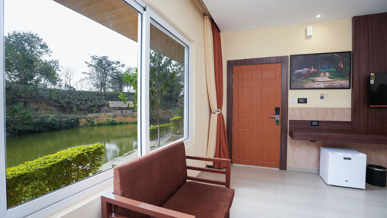 Premium Room with wooden furniture and storage, mini fridge, wall-mounted TV and lake view at Summit Green Lake Tea Resort & Spa, Kaziranga