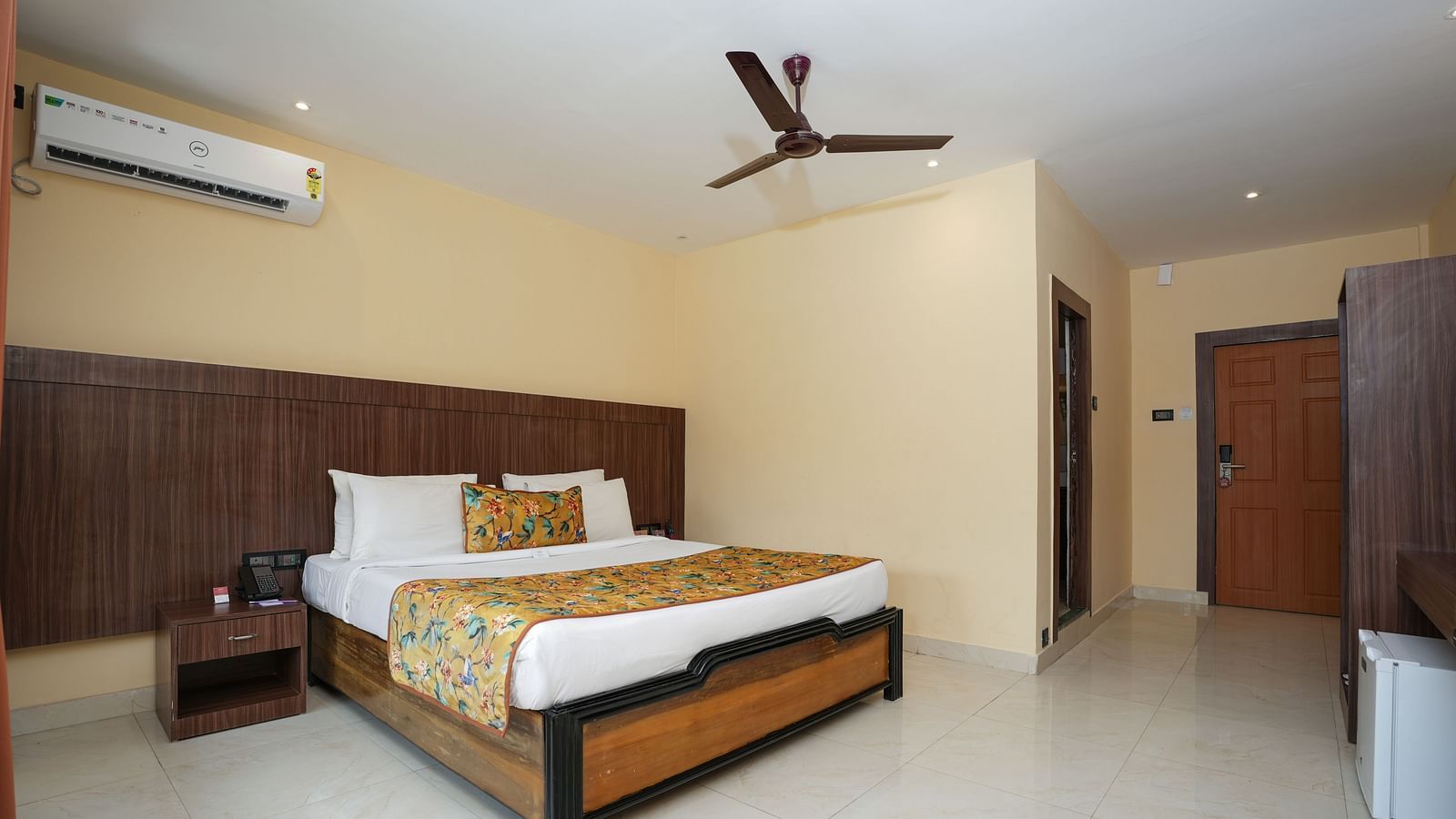 Premium room with balcony featuring a spacious bed, bedside table, wooden storage, and wall-mounted air conditioning at Summit Green Lake Tea Resort & Spa, Kaziranga