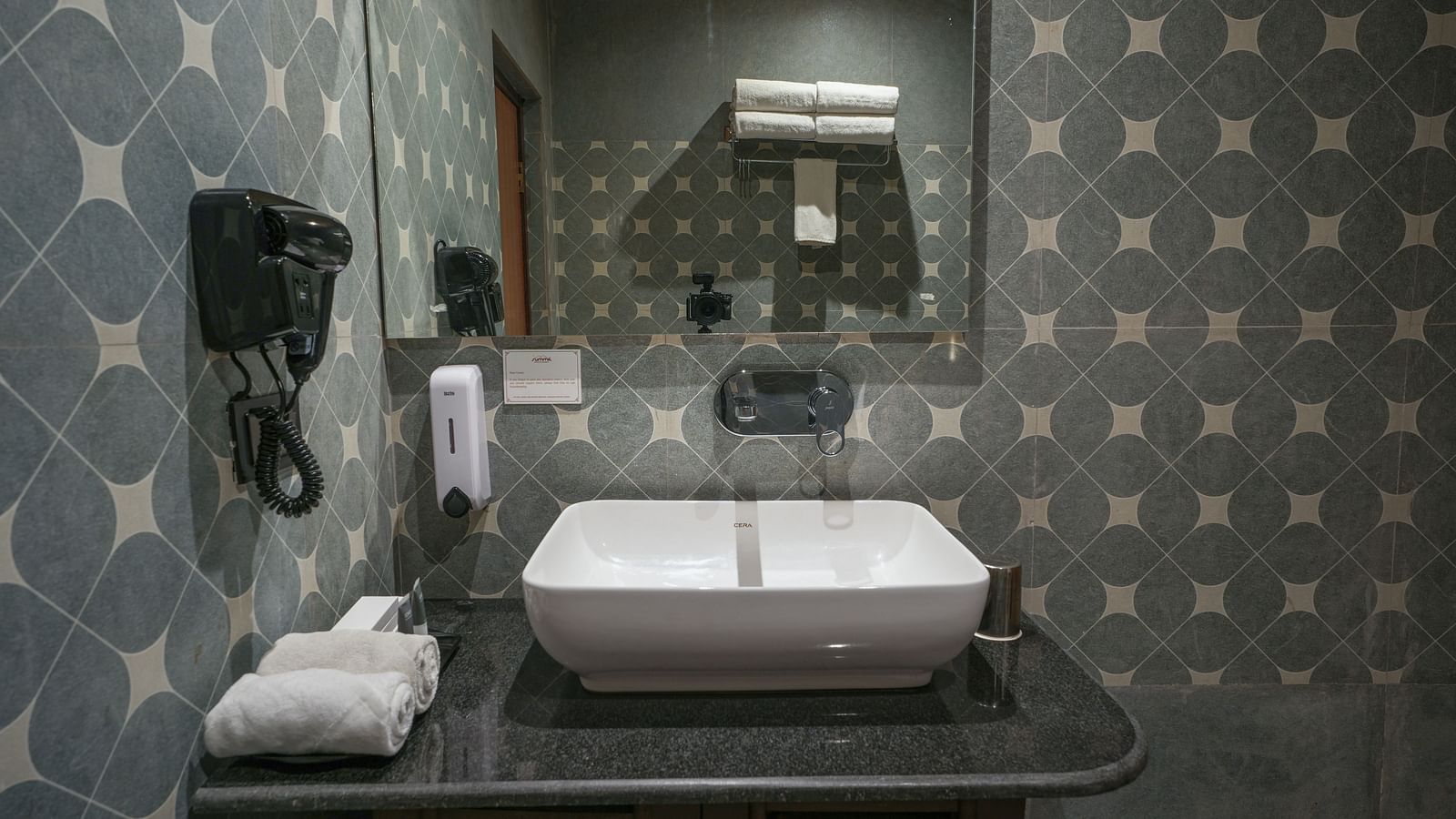 The spacious bathroom in the Premium Room includes glass-separated shower area, large washbasin with mirror, hairdryer, and wooden storage space at Summit Green Lake Tea Resort & Spa, Kaziranga