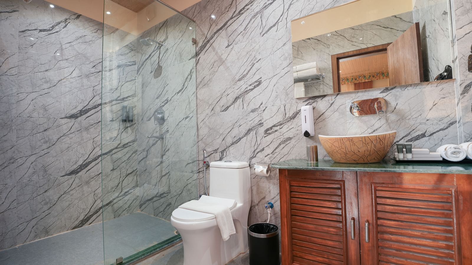 The spacious bathroom of the Bungalow  features glass separating the shower area, a large washbasin with a mirror, and wooden storage space underneath at Summit Green Lake Tea Resort & Spa, Kaziranga2