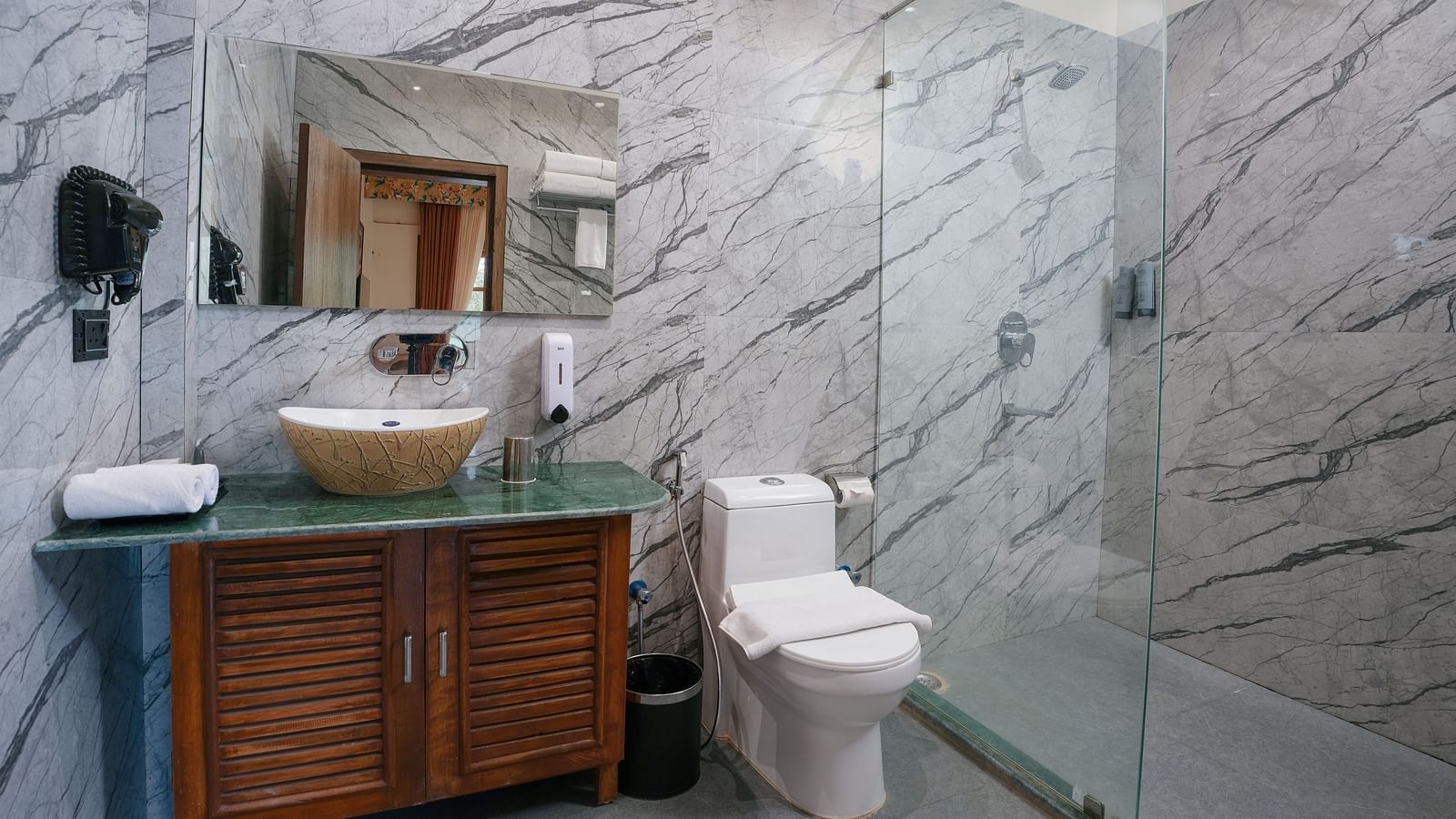 The spacious bathroom of the Bungalow  features glass separating the shower area, a large washbasin with a mirror, and wooden storage space underneath at Summit Green Lake Tea Resort & Spa, Kaziranga