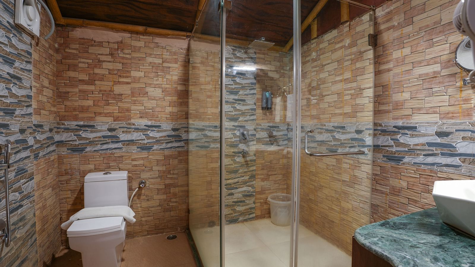 The spacious bathroom of the Ethnic villa features glass separating the shower area, a large washbasin with a mirror, and wooden storage space underneath at Summit Green Lake Tea Resort & Spa, Kaziranga