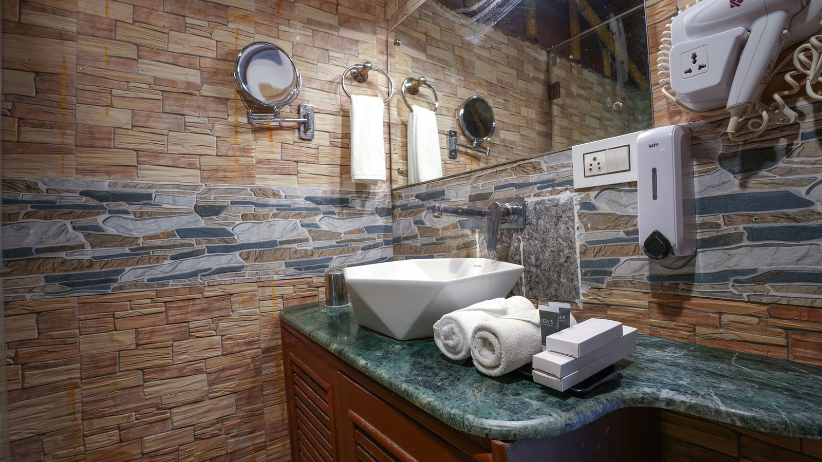 The spacious bathroom of the Ethnic villa features large washbasin with a mirror, and wooden storage space underneath at Summit Green Lake Tea Resort & Spa, Kaziranga