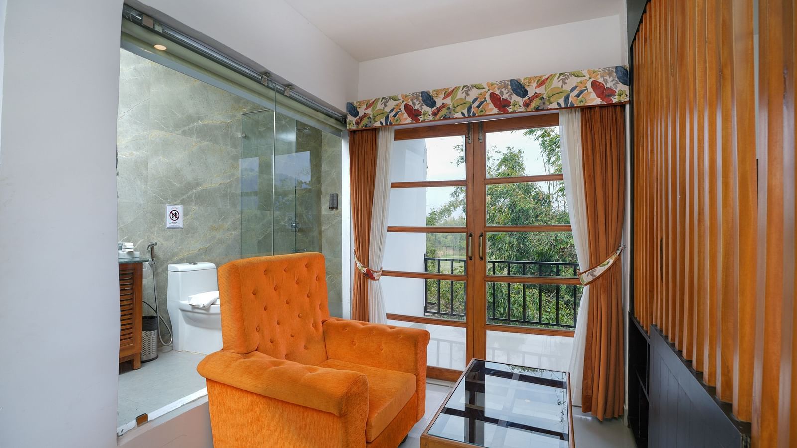 The suite with balcony features a comfortable sofa and glass table, with large doors opening to a nature view at Summit Green Lake Tea Resort & Spa, Kaziranga