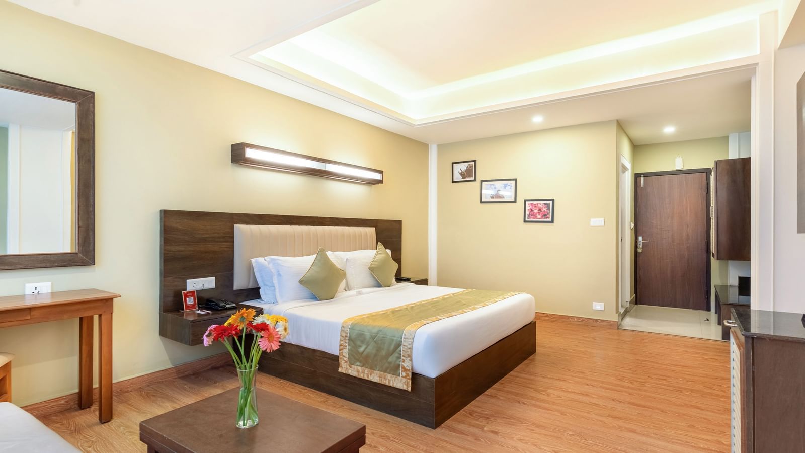 Deluxe Room at Summit North Star, Gangtok featuring double size bed, a mirror near the work desk and table and a centre table with flower vase.