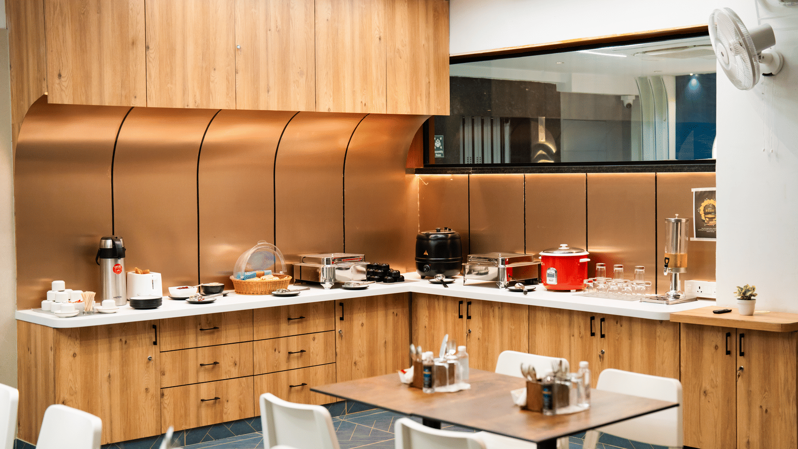 Buffet area with various dishes displayed, and tables with chairs neatly arranged in front at Sunrise Business Hotel, Hyderabad.