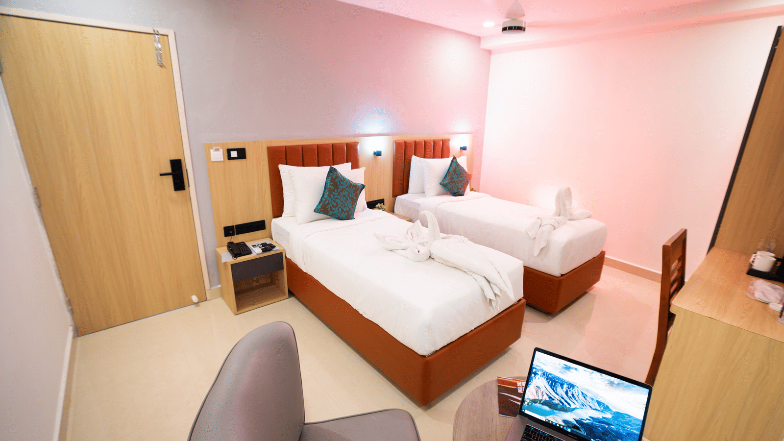 View of a room with twin beds and a laptop on a small round table with chairs on either side at Sunrise Business Hotel, Hyderabad.