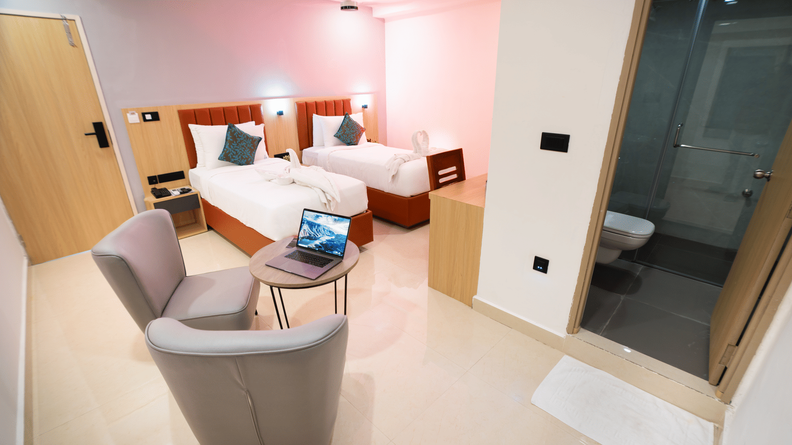 Interior of a room with twin beds, a seating area, and a doorway leading to a bathroom at Sunrise Business Hotel, Hyderabad.