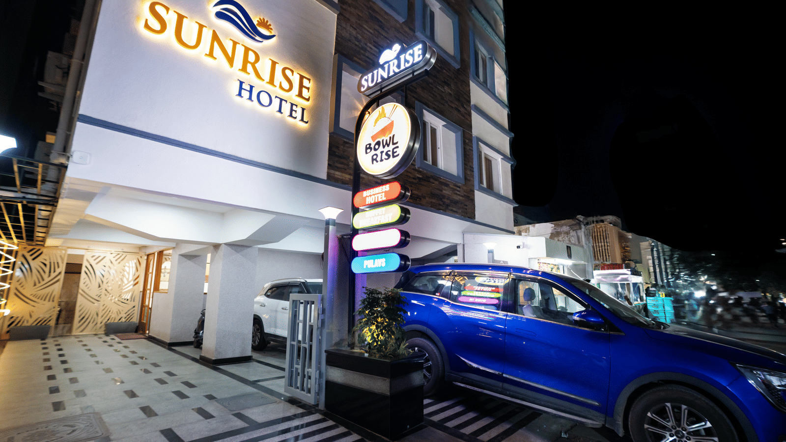 Exterior view of Sunrise Business Hotel, Hyderabad, with the signboard displaying the property name and a car parked near the entrance.