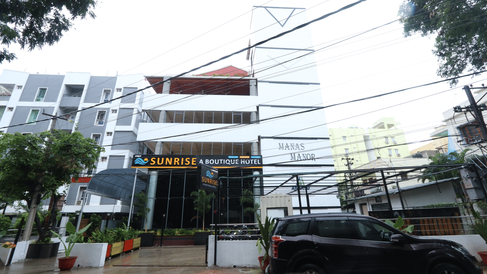 The exterior of the hotel, featuring a modern multi-storey building against a cloudy sky, with a car parked in front of the building at Sunrise A Boutique Hotel, Hyderabad.