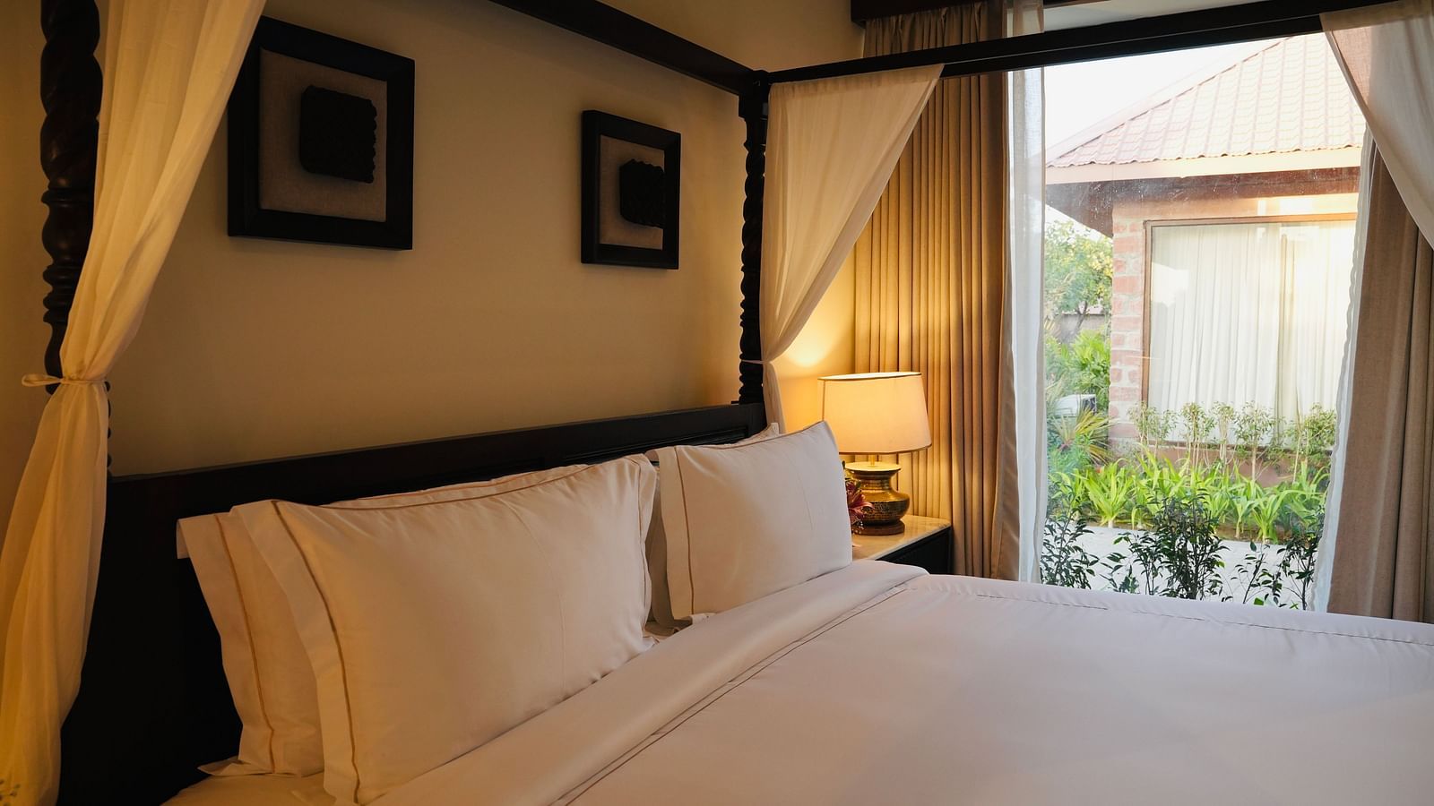 A bedroom with neatly arranged bed and photo frames on the wall and a view outside through the window.