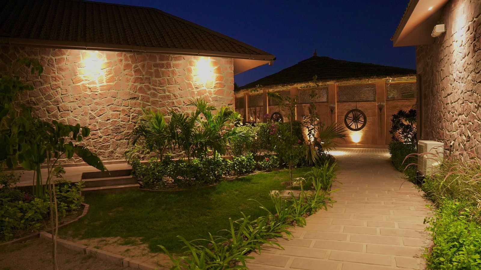 A pathway lit with lights and grass on both sides at Surpura Bagh.