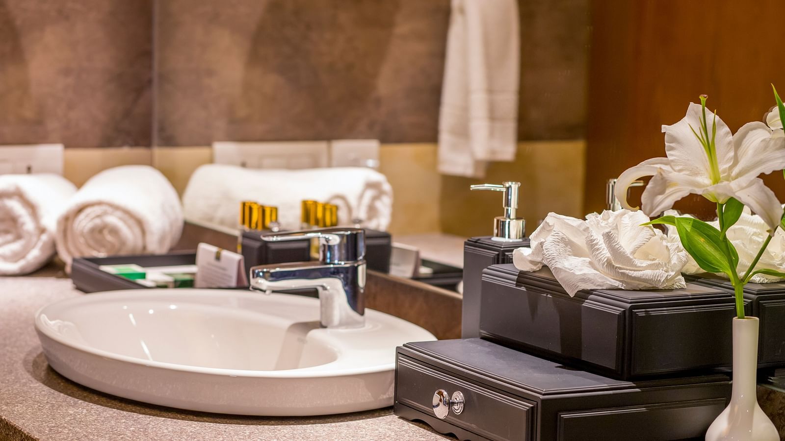 Various toiletries and towels neatly arranged near the washbasin, accompanied by a vase with decorative flowers.