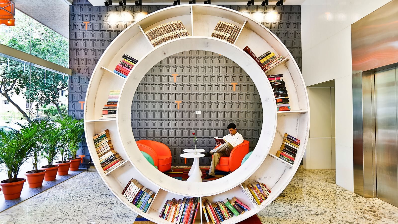 A person sitting on a sofa chair in a library with a circular book shelf placed in the centre of the room
