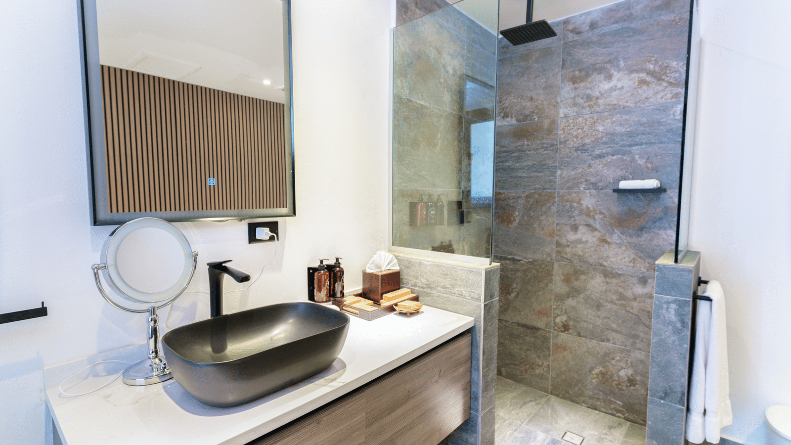 Bathroom with a freestanding bathtub, vessel sink, wall mirror, and glass-enclosed shower area at Ocean 19, Tamarind Hills Resort and Villas.