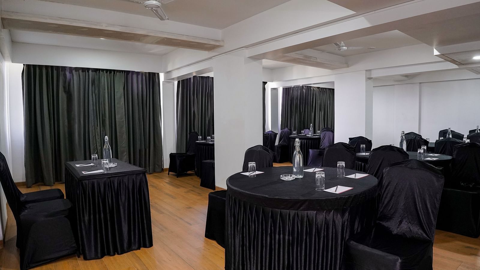 An empty conference room with round tables covered in black cloths - TGI Ameya Grand, Goa