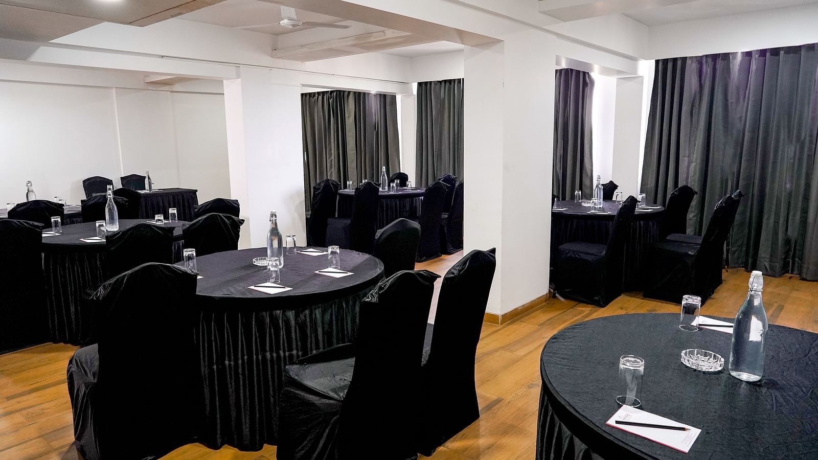 A conference room corner with black-draped tables and wooden flooring - TGI Ameya Grand, Goa