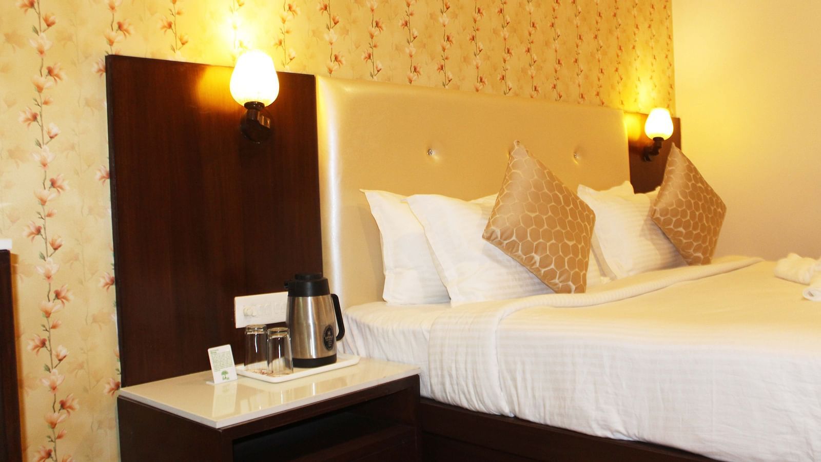 A hotel room with a beige headboard, white linens, floral wallpaper and a coffee-making station - TGI Apple Inn, Jaipur 