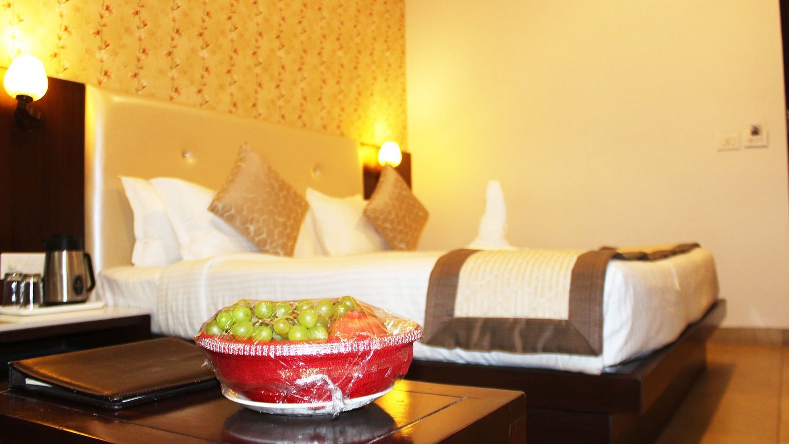 A hotel room featuring a bed with white linens, a brown runner and a bowl of fruits on the table - TGI Apple Inn, Jaipur 