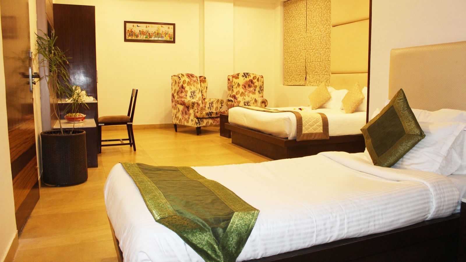 Another view of a spacious hotel room with two armchairs, a large bed with white linens and patterned wallpaper - TGI Apple Inn, Jaipur 