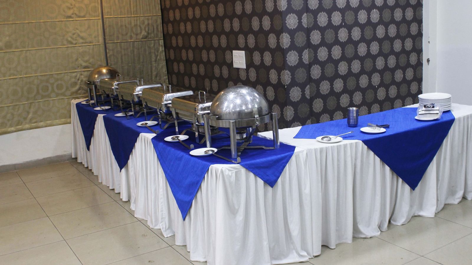 A buffet table with blue and white decorations and stainless steel chafing dishes ready for service - TGI Apple Inn, Jaipur 