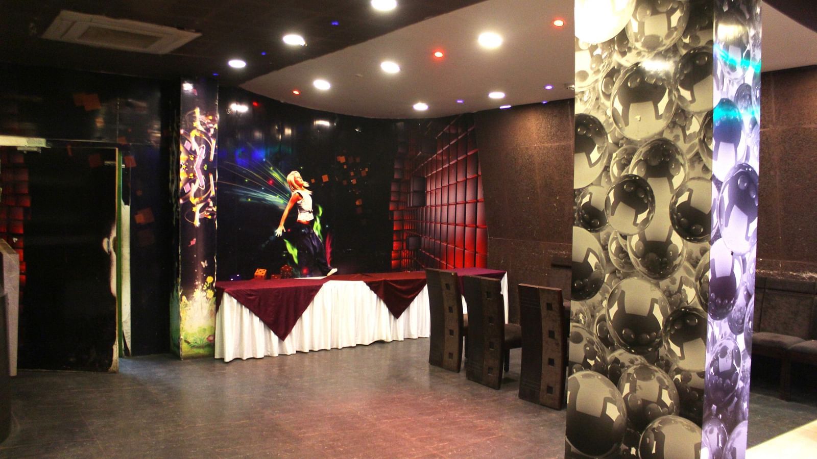 An event space with dark ambience, spotlights and a mural of a dancer on the wall - TGI Apple Inn, Jaipur 