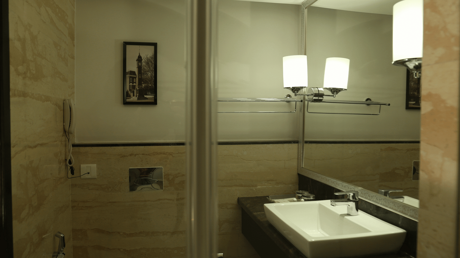 A bathroom interior with modern amenities featuring a large mirror above a white rectangular sink - TGI Grand Fortuna, Hosur